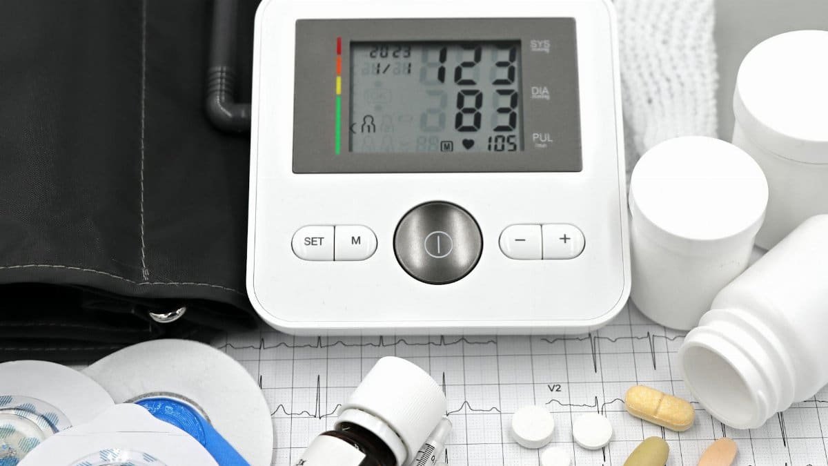 Close-up of medical equipment including blood pressure monitor, pills, and ECG printout.