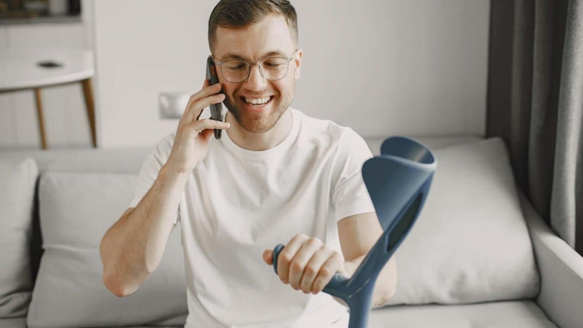 Man using crutch smiling and talking on phone indoors.