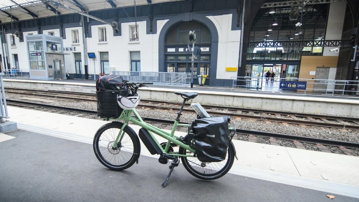A green cargo bike parked at a railway station platform in France, highlighting sustainable travel.