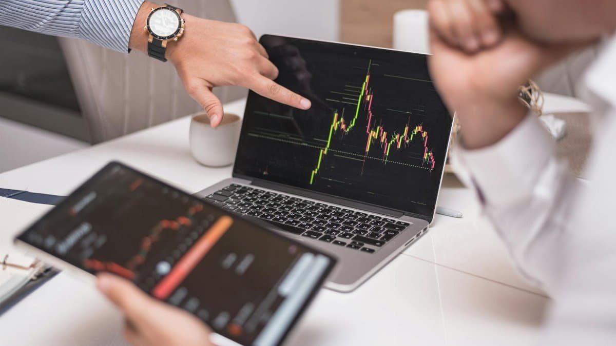 Business professionals analyzing cryptocurrency market trends on laptop and tablet.