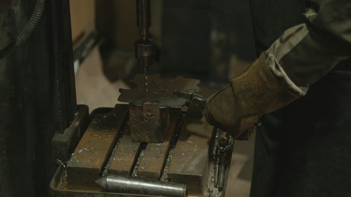 A blacksmith operates a drill press to craft a metal piece indoors with precision.