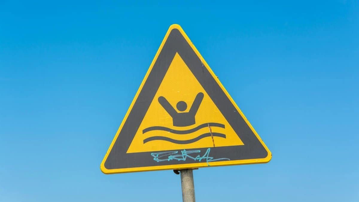 Yellow triangular warning sign for swimming area under a clear blue sky.