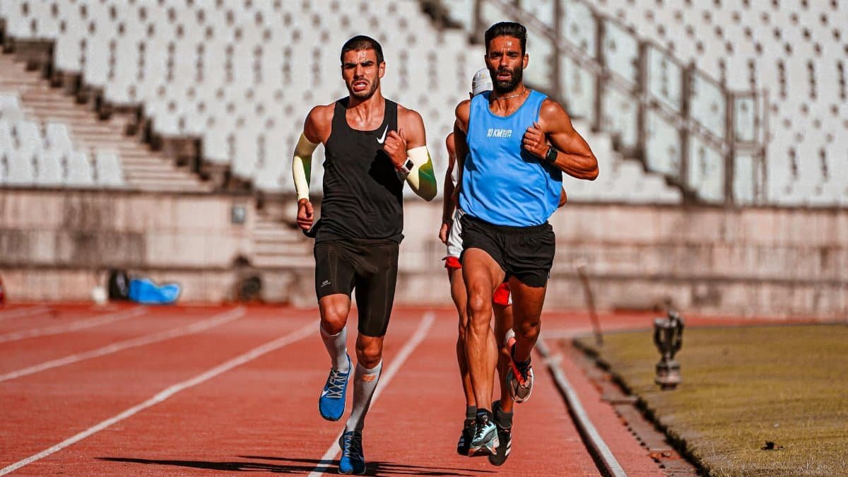 Two male runners competing on a stadium track during a sunny day.