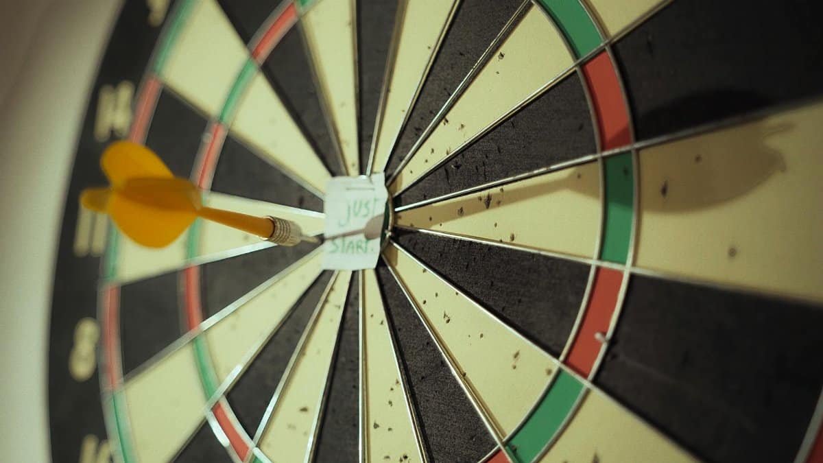 Close-up of a yellow dart hitting the bullseye on a dartboard with a motivational note.