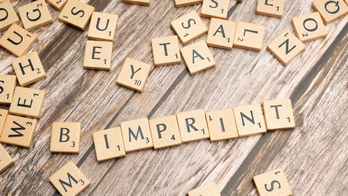 Wooden Scrabble tiles arranged on a wooden surface, spelling 'Imprint'.