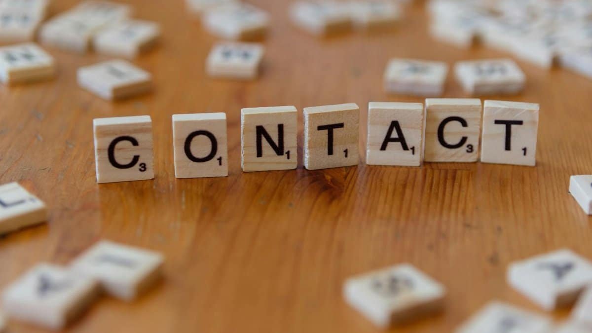 Scrabble letters spelling 'contact' on a wooden table surface.