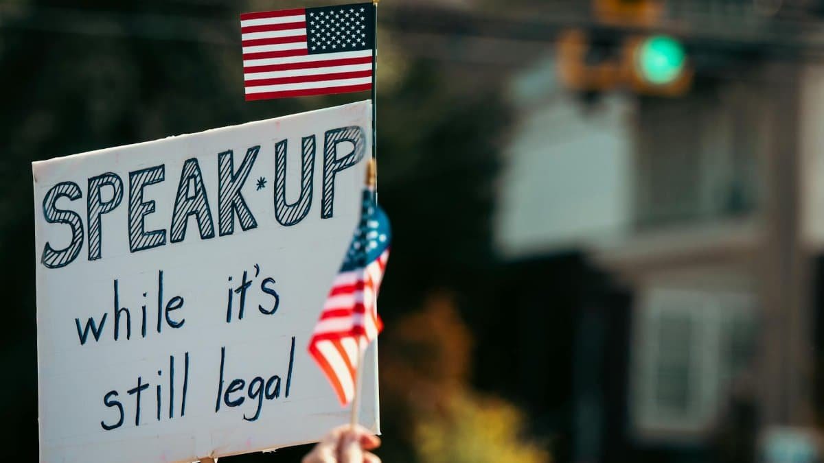 Protest sign with the message and American flag at a rally, highlighting free speech themes.