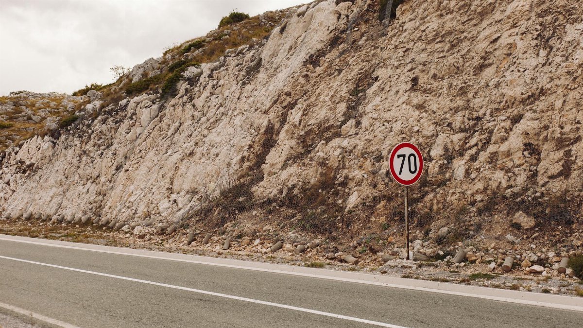 A tarmac road along rocky terrain with a 70 speed limit sign on a cloudy day.