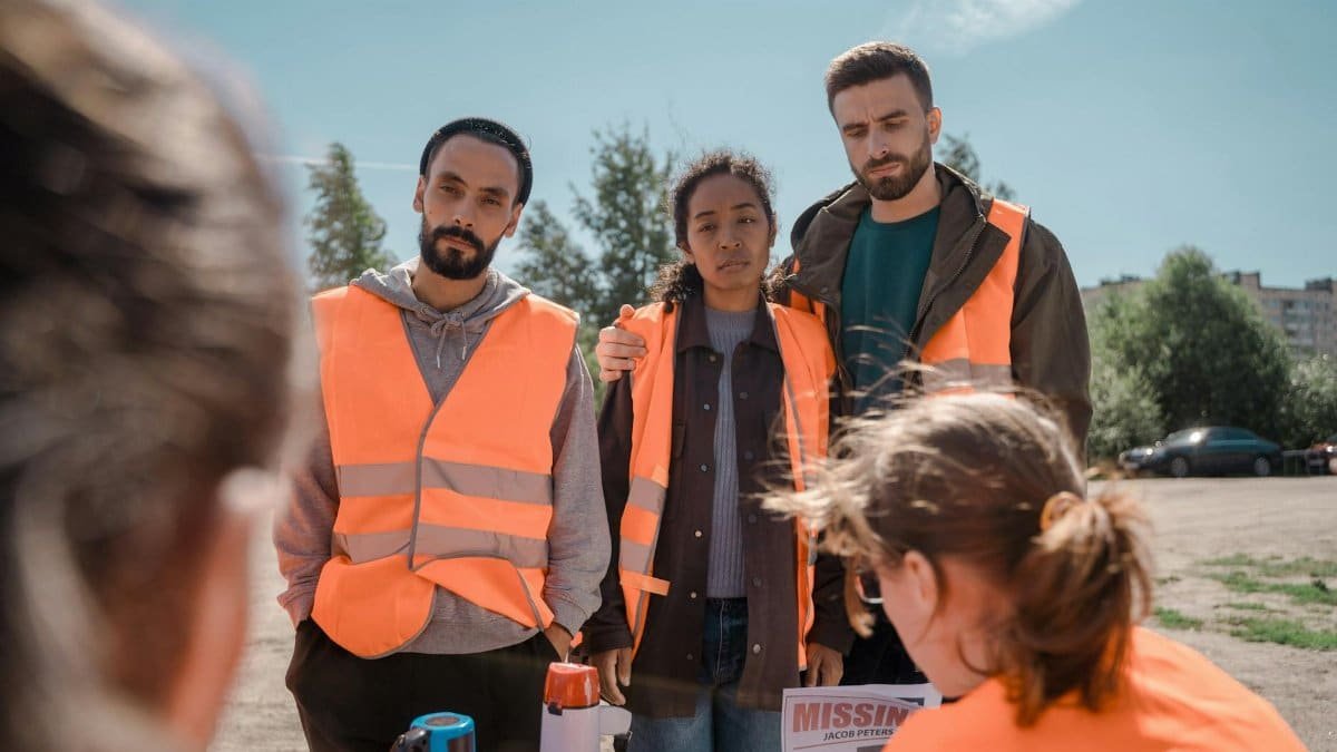 Group of volunteers wearing orange vests coordinating efforts outdoors on a sunny day.