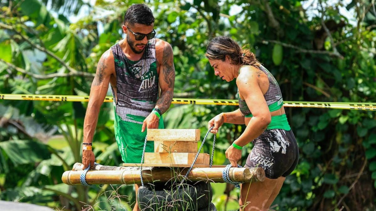 Two adults engage in a challenging outdoor team-building exercise with wooden obstacles.