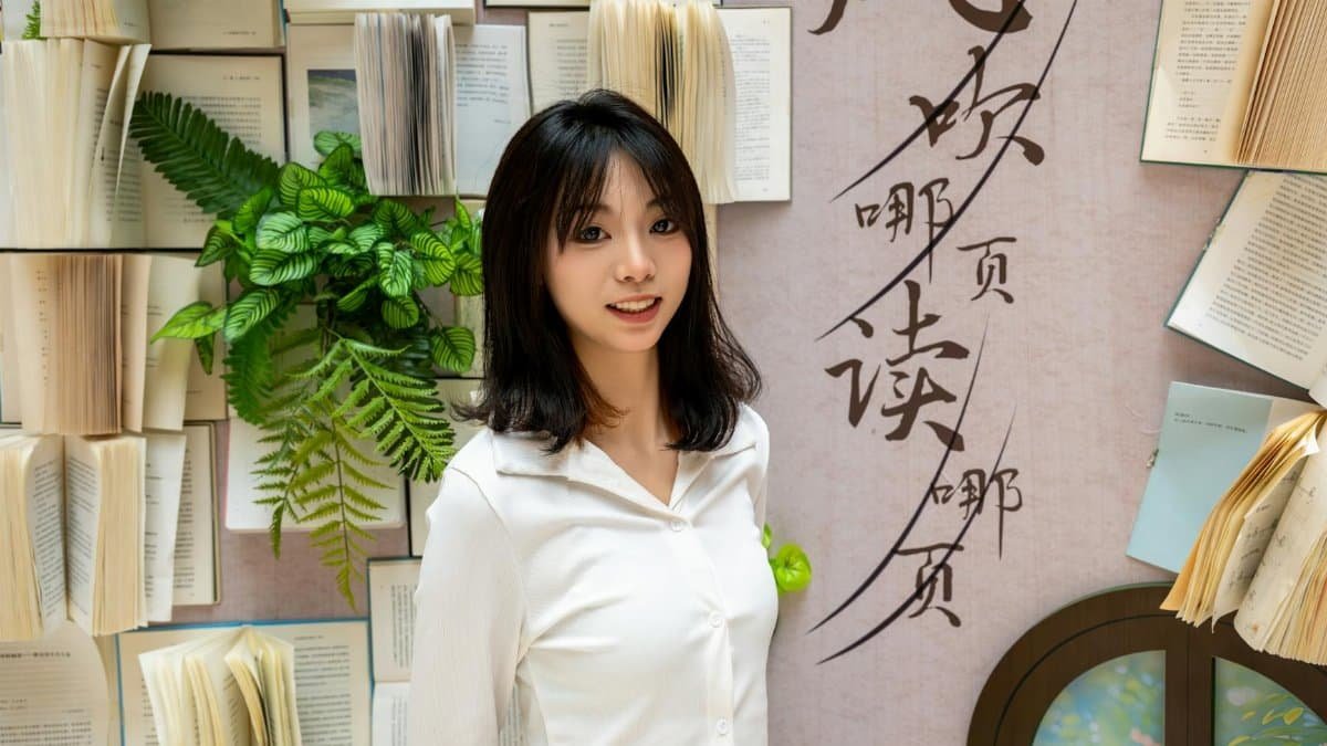Portrait of a smiling woman with open books and plants on a decorative wall.