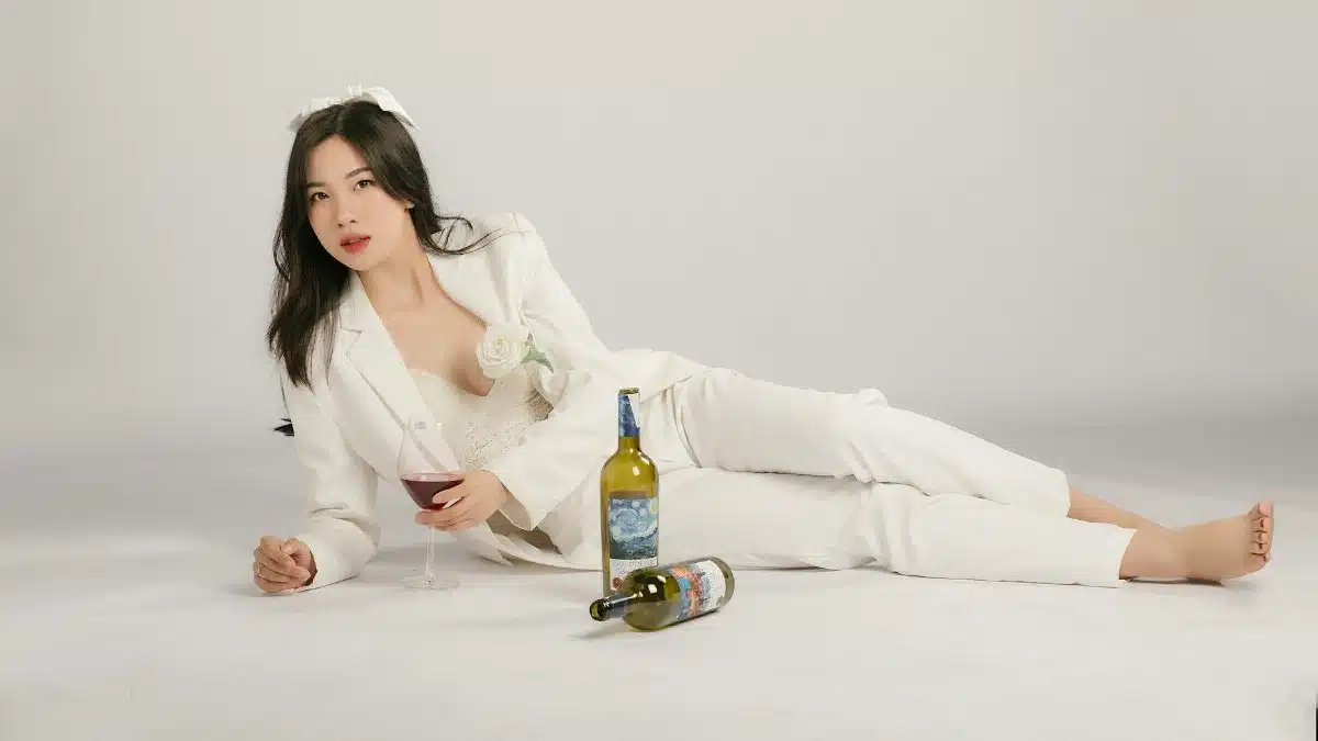 Stylish asian woman posing with wine bottles on white background in Hà Nội.