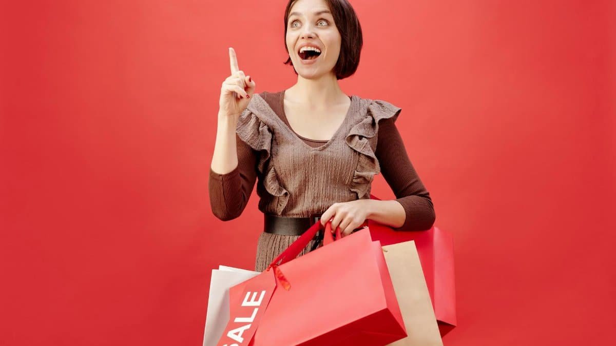 Cheerful woman with shopping bags celebrating a sale on a vibrant red backdrop.