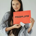 Smiling woman holds a red 'REBajas' sign, promoting sales and discounts.