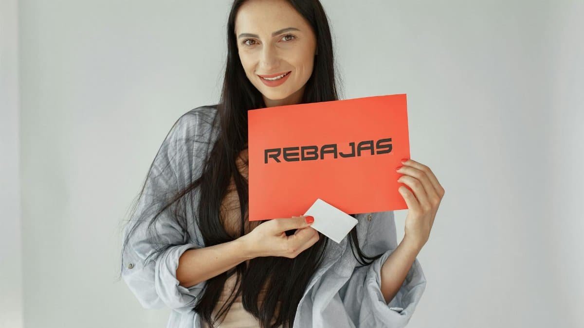 Smiling woman holds a red 'REBajas' sign, promoting sales and discounts.