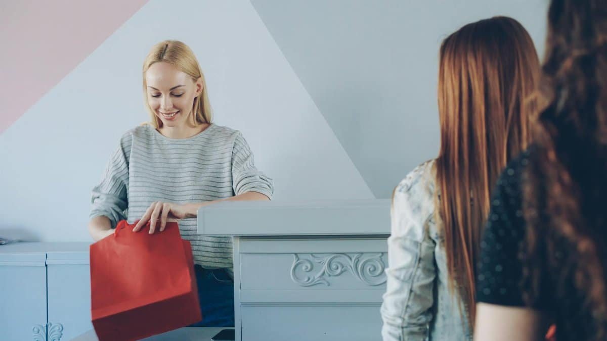 Confident cashier handling a colorful red shopping bag for customers in a vibrant store.