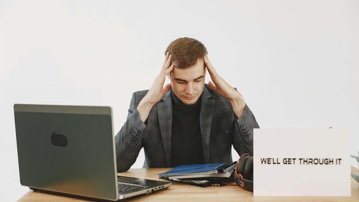 Young man in home office feeling stressed, working during pandemic with motivational message by his side.