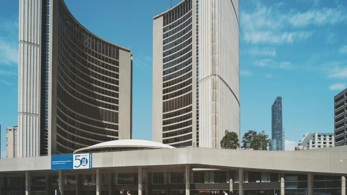 Iconic Toronto City Hall with adjacent buildings under a clear blue sky, capturing urban architecture.