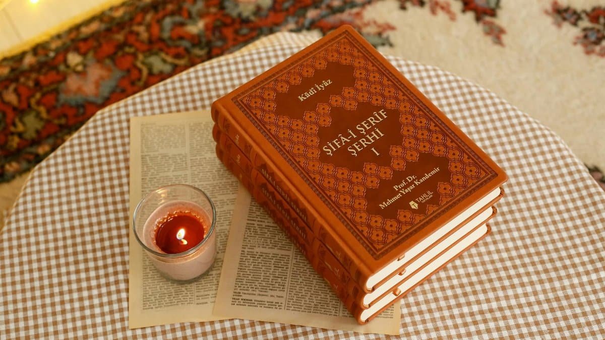 Warm ambiance with a candle beside stacked books on a checkered tablecloth.