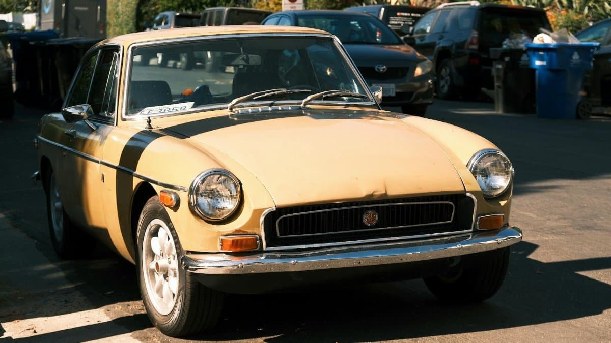 Classic yellow MGB coupe parked on a city street, highlighting vintage automotive charm.