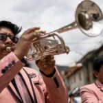Two musicians in pink suits play brass instruments during an outdoor parade in Tarma, Peru.