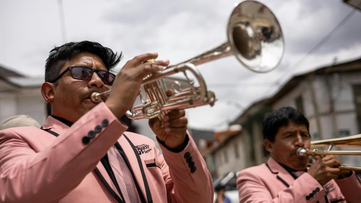 Two musicians in pink suits play brass instruments during an outdoor parade in Tarma, Peru.