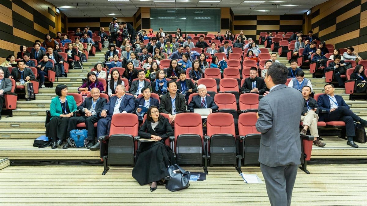 Professional setting of a business conference with attendees and a presenter in an auditorium.