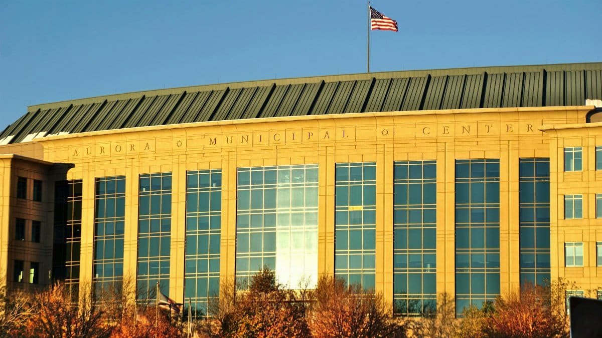 Aurora Municipal Center building with waving American flag in daylight.