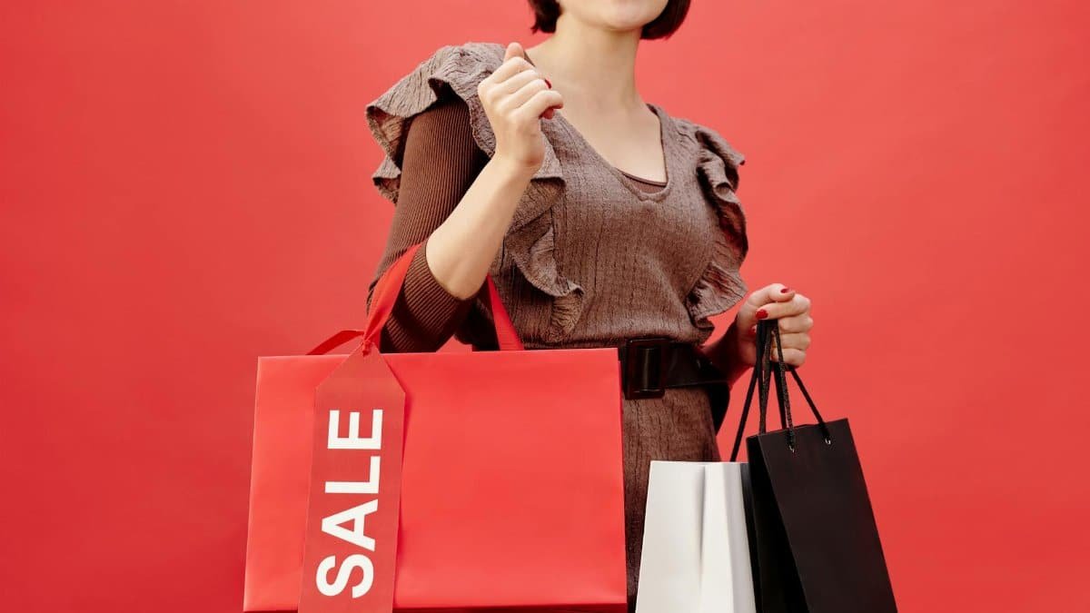 Smiling woman holding sale shopping bags against vibrant red backdrop.