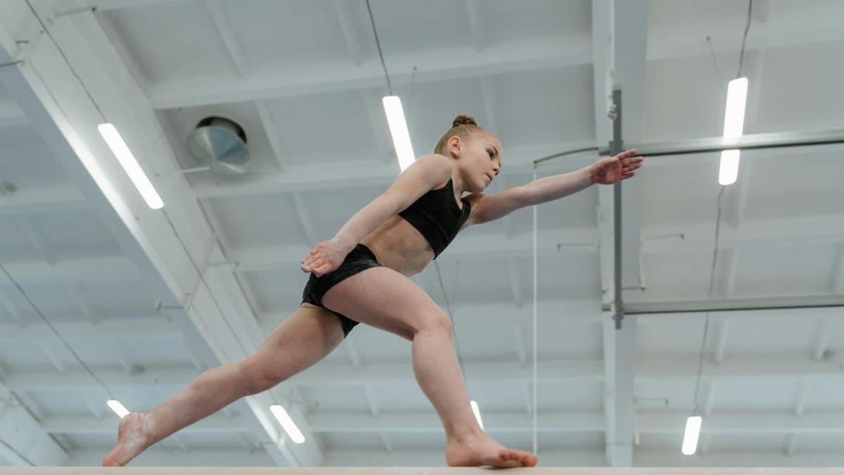Child gymnast performing balancing act on beam in a gymnasium setting.