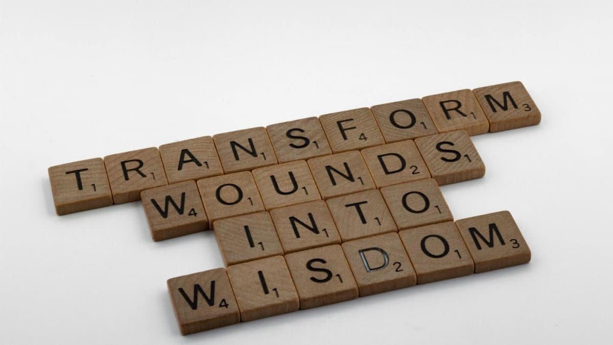 Wooden Scrabble tiles spelling 'Transform Wounds into Wisdom' on a neutral background.