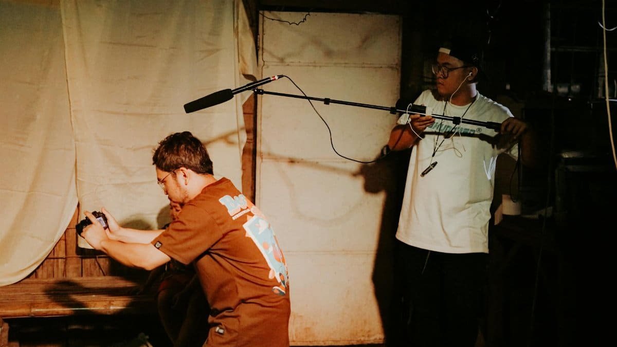 Two adults engaged in a live performance setup with camera and microphone indoors.