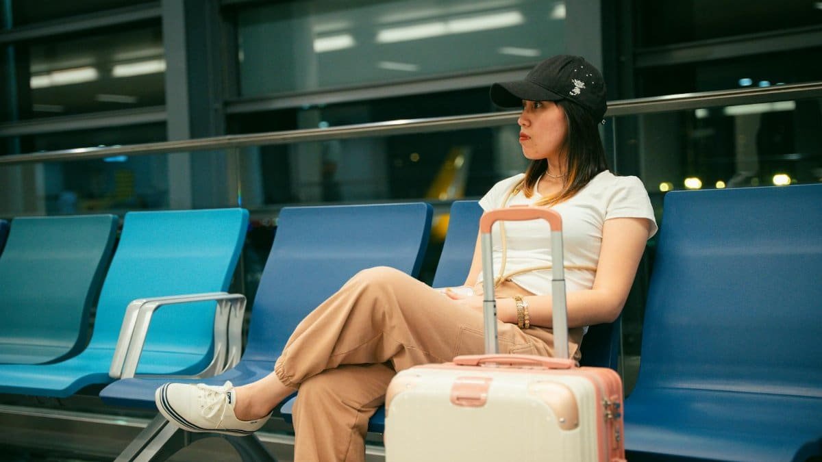 Young woman sitting in airport with luggage, anticipating travel. Casual travel attire.