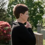 A woman dressed in black stands solemnly in a peaceful cemetery, reflecting amidst gravestones.
