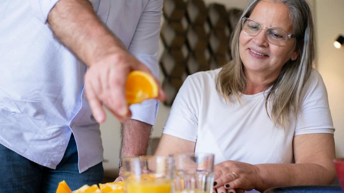A senior woman smiles while an orange is squeezed for fresh juice at home.