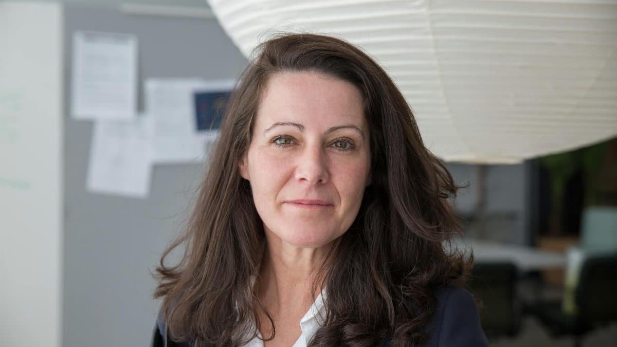 Portrait of a confident businesswoman in a modern office, wearing a blazer with a neutral expression.