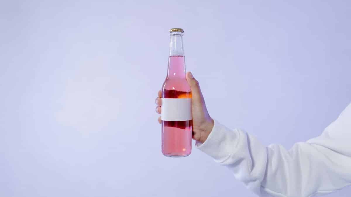 Close-up shot of a pink beverage bottle held by a hand against a light background.