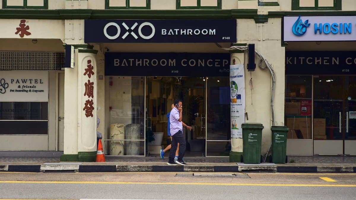 Man walking past storefronts in colorful Singapore street, featuring OXO Bathroom.