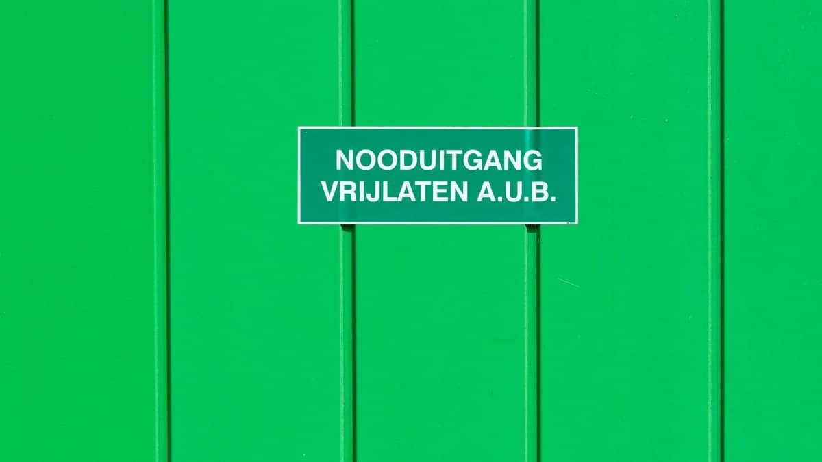 A green metal wall featuring an emergency exit sign in Dutch. Perfect for safety-themed graphics.