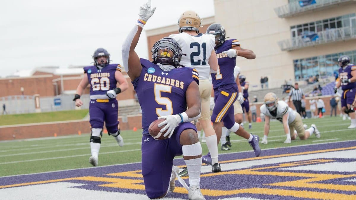 A passionate football player kneels in celebration on the field during a competitive match.