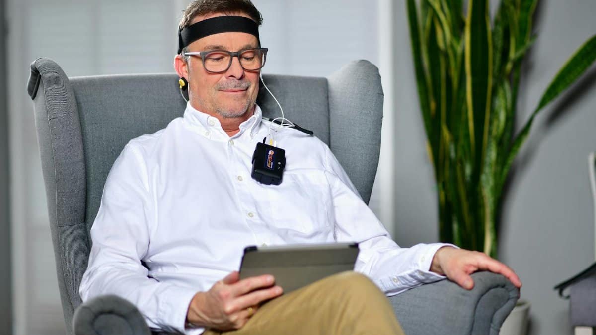 Man sitting in an armchair using a neurofeedback device, illustrating modern technology in healthcare.