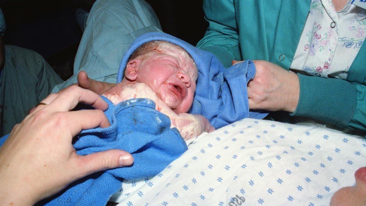 A newborn baby immediately after birth being wrapped in a hospital delivery room.