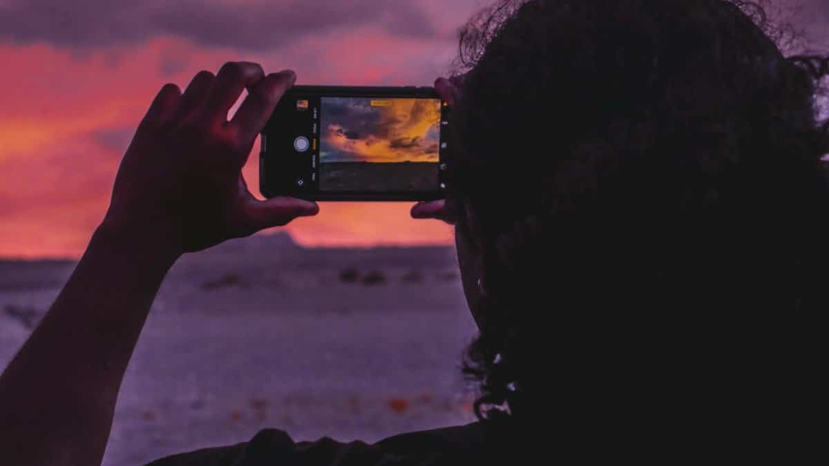 Silhouette of a person photographing a stunning sunset with a smartphone, creating an artistic frame.