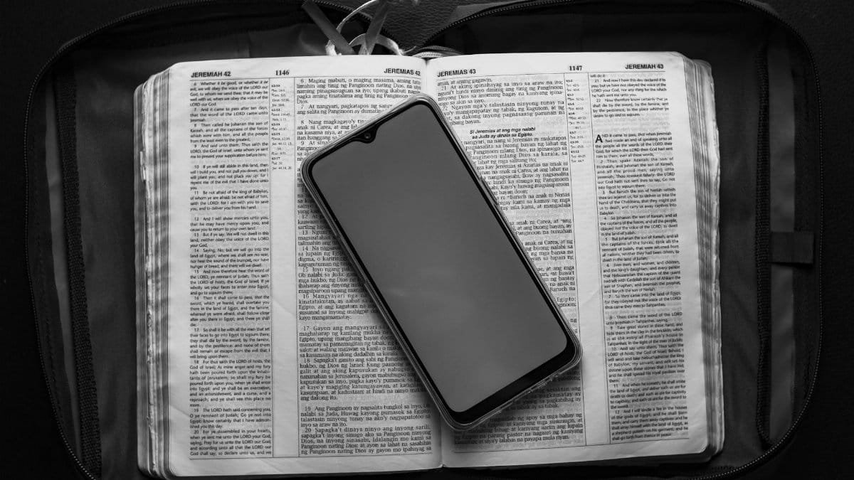 Top view of modern cellphone with empty screen placed on opened textbook in case bag