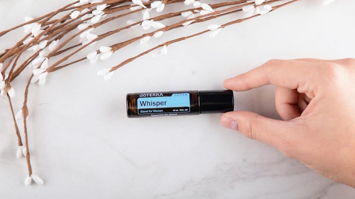 Hand holding a doterra essential oil bottle with a spring floral arrangement on a marble surface.