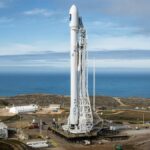 A SpaceX rocket stands on a launch pad overlooking the ocean under a clear sky.