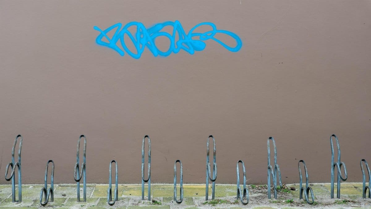 An empty bicycle rack with blue graffiti on a brown wall, creating urban texture.