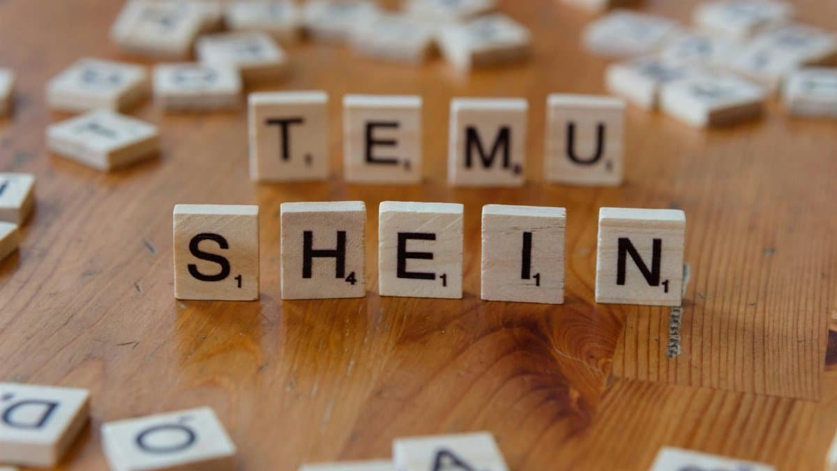 Scrabble tiles spelling 'TEMU SHEIN' on a wooden table, representing fashion brands.