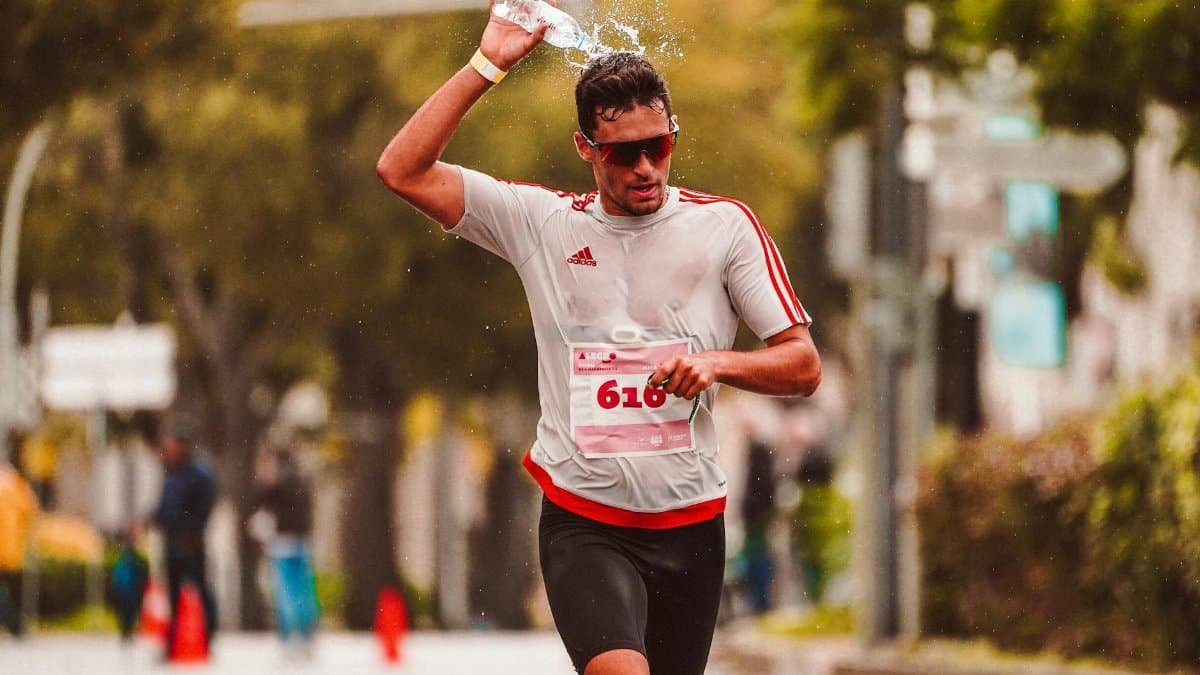 Marathon athlete pouring water over his head to cool down during an intense run.