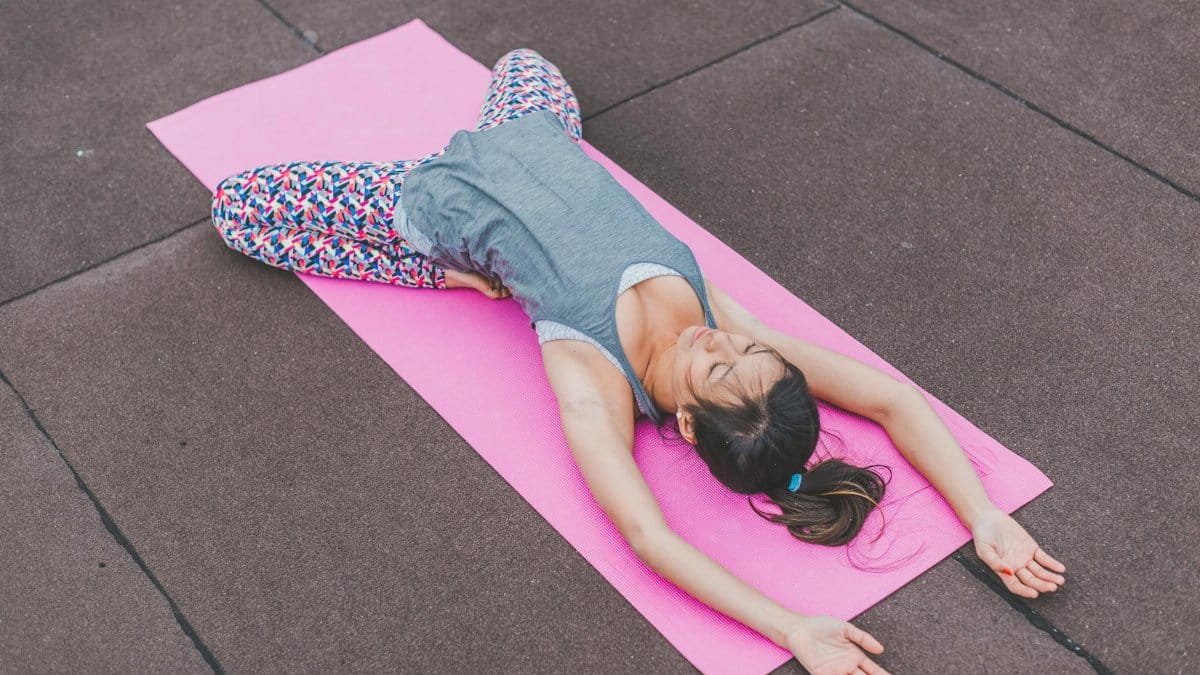 Woman performing yoga stretch on a pink mat outdoors. Promotes fitness and relaxation.